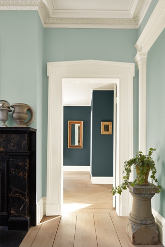 Light green painted hallway with wood floors leads to a room with bold teal walls and decorative mirrors.
