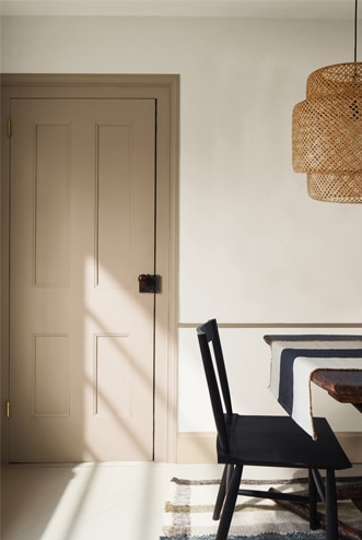 Neutral-painted dining room featuring a tan door, dark wood dining table, and black chair.