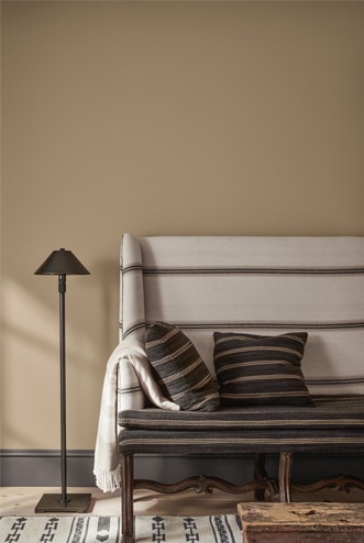 A bench upholstered in white fabric with black stripes and coordinating pillows against a tan wall, with a black floor lamp.