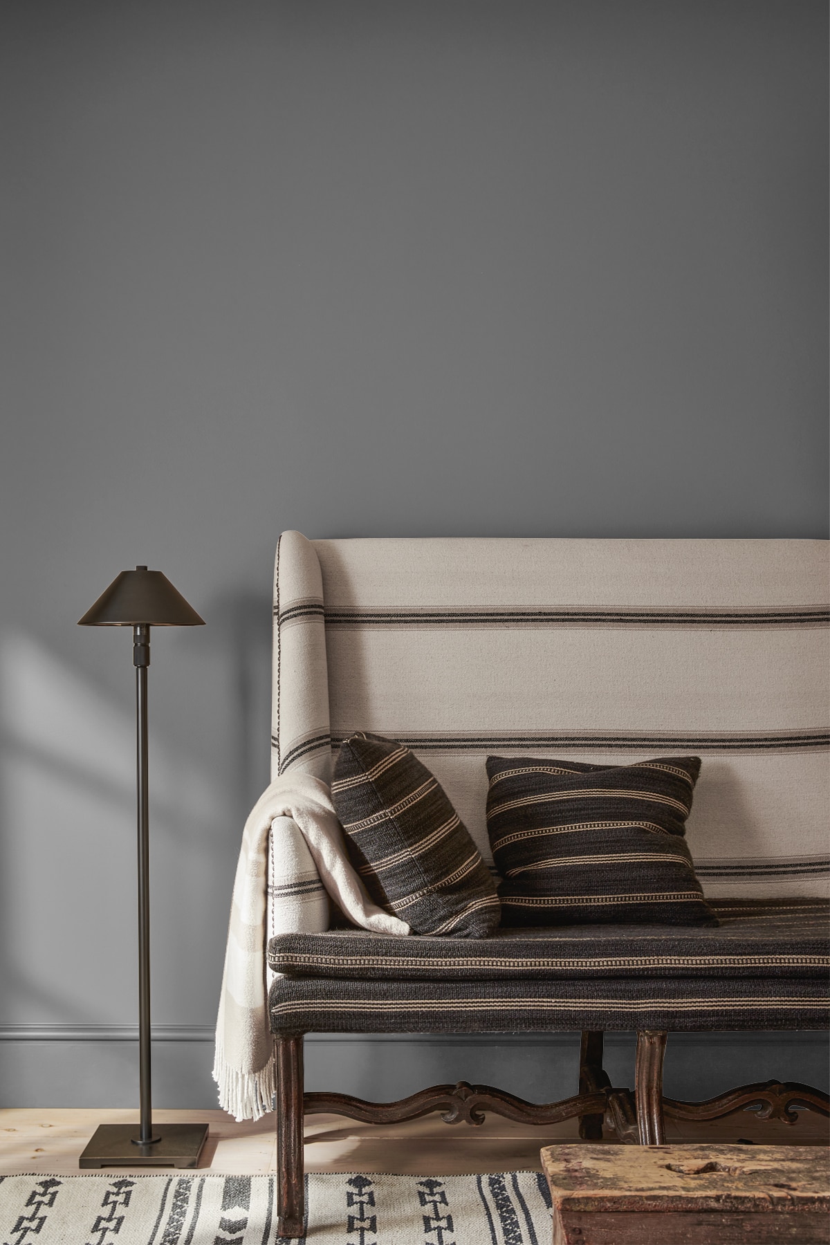 A bench upholstered in white fabric with black stripes and coordinating pillows against a tan wall, with a black floor lamp.