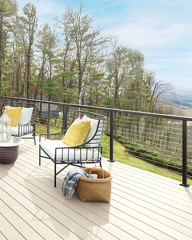 Jolis meubles de jardin rembourrés blancs avec coussins décoratifs jaunes et petite table sur une terrasse enduite de teinture Woodluxe au fini opaque de couleur Tonnelle Blanche ES-01.
