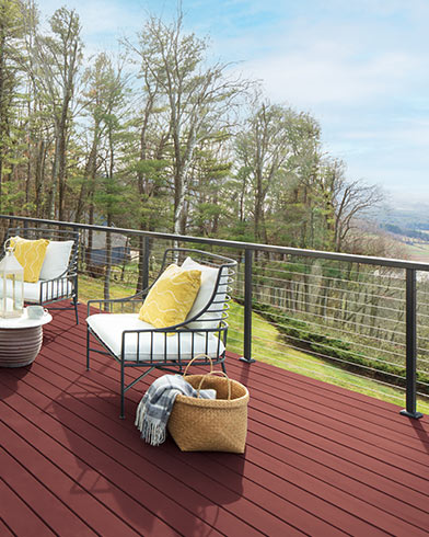 Bonitos muebles de exterior acolchados de color blanco con almohadones amarillos y una mesa pequeña en una terraza teñida con Woodluxe® liso en color Rojo Granero ES-22.