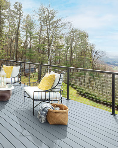 Jolis meubles de jardin rembourrés blancs avec coussins décoratifs jaunes et petite table sur une terrasse enduite de teinture Woodluxe au fini opaque de couleur Bleu Celtique ES-31.