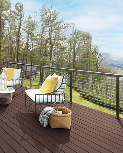 Bonitos muebles de exterior acolchados de color blanco con almohadones amarillos y una mesa pequeña en una terraza teñida con Woodluxe® liso en color Caoba ES-60.