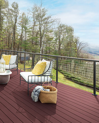 Pretty white cushioned outdoor furniture with yellow pillows and a small table on a New Pilgrim Red ES-21 Woodluxe® Solid stained deck.
