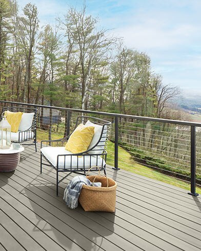 Jolis meubles de jardin rembourrés blancs avec coussins décoratifs jaunes et petite table sur une terrasse enduite de teinture Woodluxe au fini opaque de couleur Gris Goéland Argenté ES-72.