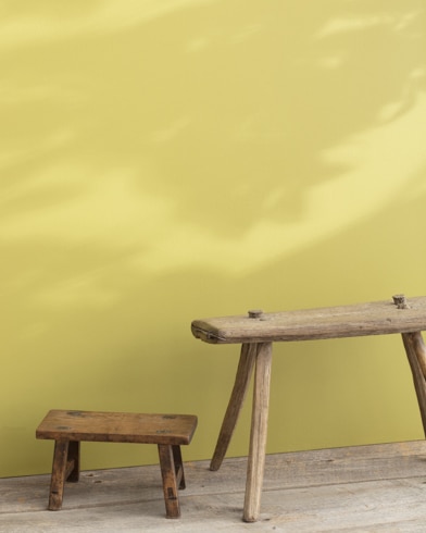 Two wooden stools, one large and one small, appear in front of a wall painted Wasabi.
