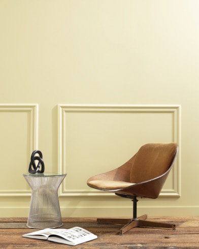 A flat wood riser holds a curved wooden chair, glass vase and open book in front of a paneled wall painted Castelton Mist.