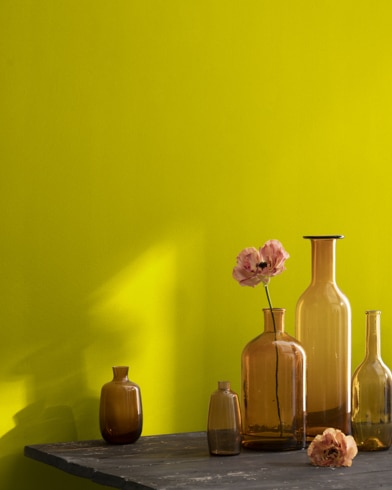 A collection of brown-tinted glass vases sit atop a wooden shop table next to a wall painted Chartreuse.