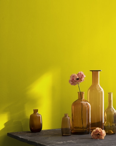 A collection of brown-tinted glass vases sit atop a wooden shop table next to a wall painted Eve Green.
