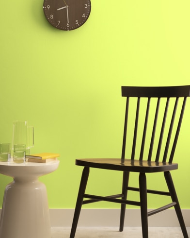 A brown clock hangs on a Apple Green-painted wall above a dark wood chair and small dining table.