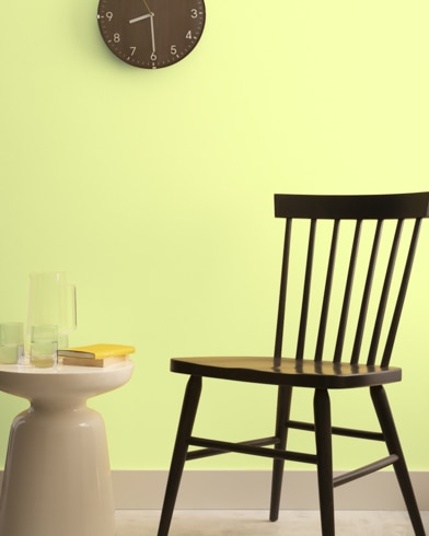 A brown clock hangs on a Fresh Cut Grass-painted wall above a dark wood chair and small dining table.
