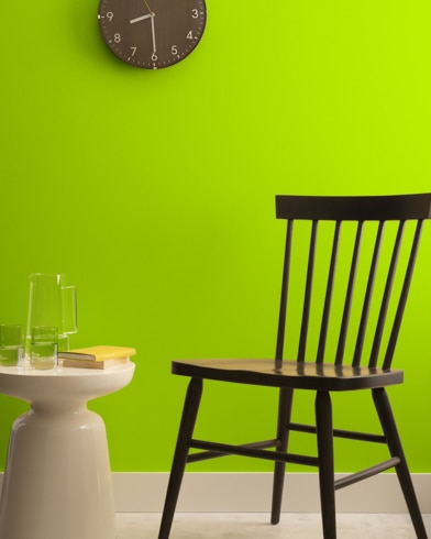 A brown clock hangs on a Lime Green-painted wall above a dark wood chair and small dining table.