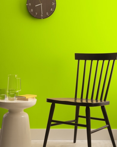 A brown clock hangs on a Magartita-painted wall above a dark wood chair and small dining table.