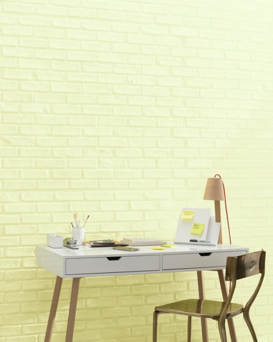 A white and copper writing desk and a bronze metal chair sit in front of a brick wall painted Celadon Green.