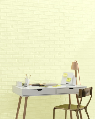 A white and copper writing desk and a bronze metal chair sit in front of a brick wall painted Lime Ricky.
