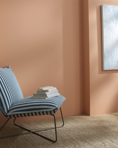 Una pared pintada de Cervato Pastando detrás de un sillón sin apoyabrazos a rayas con libros encima.