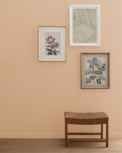 A Dearborn Tan-painted wall with three framed art pieces, a small bench, and a floor lamp.