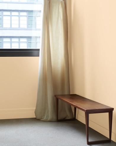 In a Sepia Tan-painted room with a wooden bench, a gauzy white curtain hangs next to an open window.