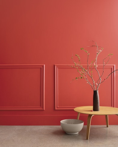 A midcentury wooden accent table and decor in front of a Claret Rose-painted wall with rectangular molding.