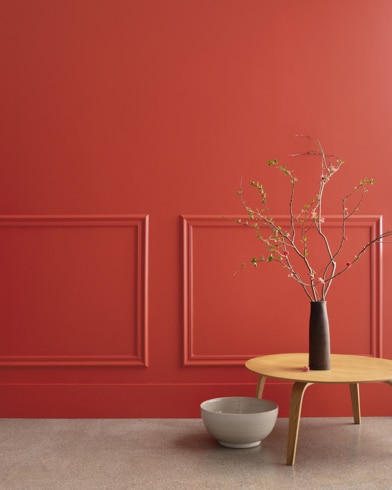 A midcentury wooden accent table and decor in front of a Cornwallis Red-painted wall with rectangular molding.