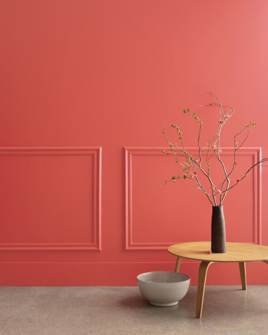 A midcentury wooden accent table and decor in front of a Raspberry Blush-painted wall with rectangular molding.