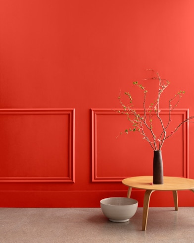 A midcentury wooden accent table and decor in front of a Ravishing Red-painted wall with rectangular molding.