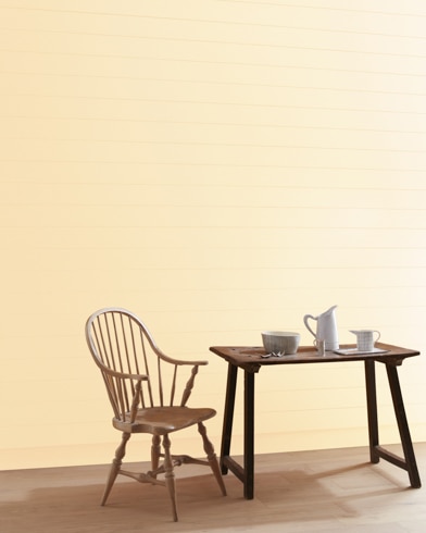 A Citrus Mist-painted wall with wooden spindle chair and white pitcher, cup and bowl on a table.