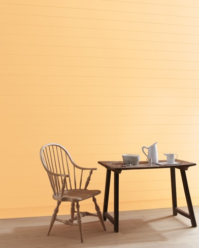 A Honey Burst-painted wall with wooden spindle chair and white pitcher, cup and bowl on a table.