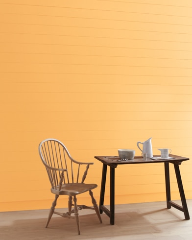 A Honeybell-painted wall with wooden spindle chair and white pitcher, cup and bowl on a table.