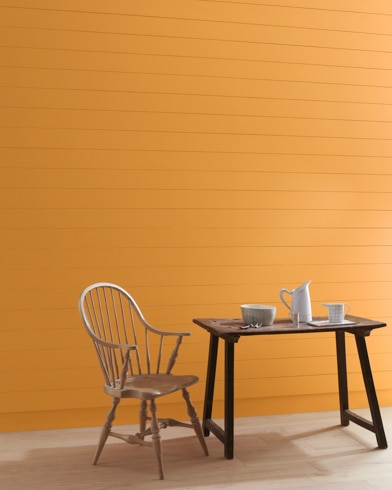An Autumn Orange-painted wall with wooden spindle chair and white pitcher, cup and bowl on a table.