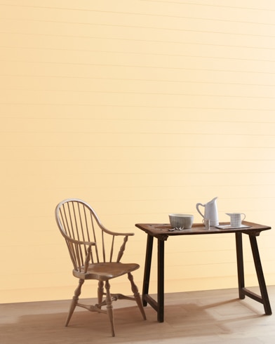 A Pineapple Smoothy-painted wall with wooden spindle chair and white pitcher, cup and bowl on a table.