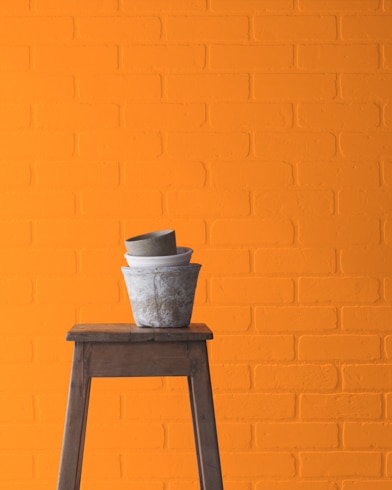A Citrus Orange-painted brick wall behind a wooden stool with planting pots on top.