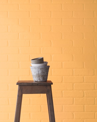 A Marmalade-painted brick wall behind a wooden stool with planting pots on top.