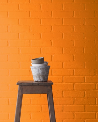A Startling Orange-painted brick wall behind a wooden stool with planting pots on top.