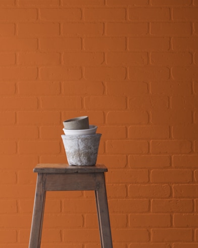 A Tandoori-painted brick wall behind a wooden stool with planting pots on top.
