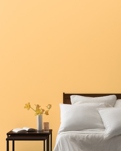 A Florida Orange-painted bedrom wall, bed with white linens, and a night stand.