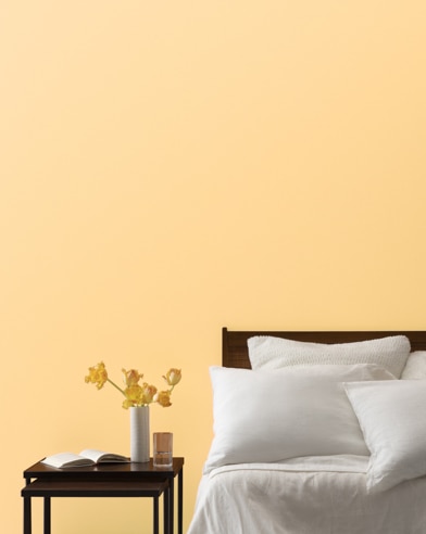 An Orange Froth-painted bedroom wall, bed with white linens, and a night stand.