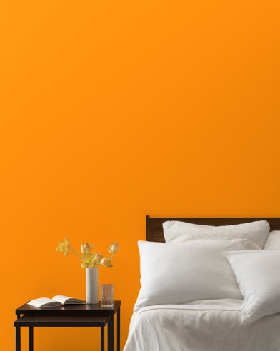 An Orange Juice-painted bedroom wall, bed with white linens, and a night stand.
