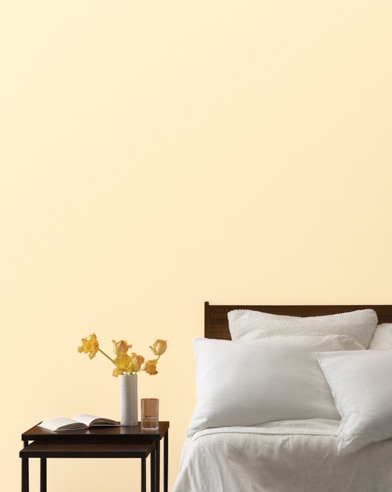 A Pale Daffodil-painted bedroom wall, bed with white linens, and a night stand.