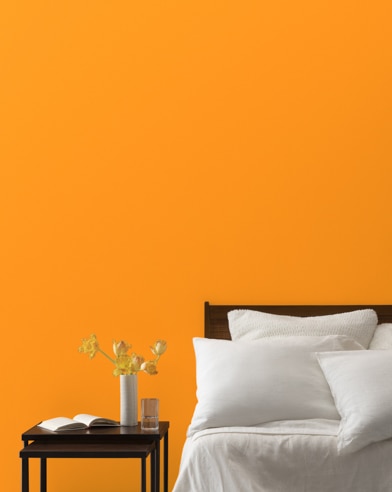 A Sharp Cheddar-painted bedroom wall, bed with white linens, and a night stand.