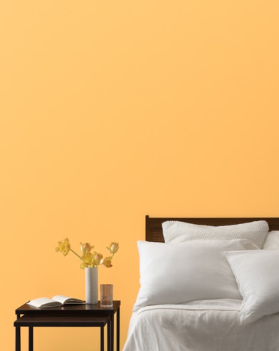 A Sweet Orange-painted bedroom wall, bed with white linens, and a night stand.