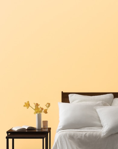 A Yellow Haze-painted bedroom wall, bed with white linens, and a night stand.