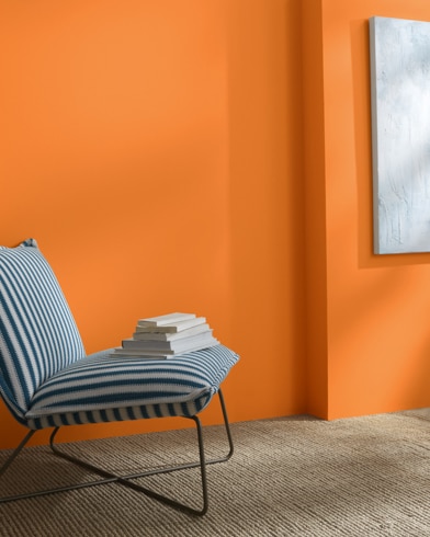 A Fruit Punch-painted wall behind a striped armless lounge chair with books on it. 