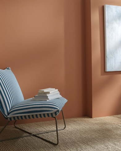 Una pared pintada de Pensando en Georgia detrás de un sillón sin apoyabrazos a rayas con libros encima.