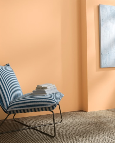 A Peach Pudding-painted wall behind a striped armless lounge chair with books on it. 