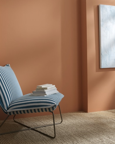 A Potters Clay-painted wall behind a striped armless lounge chair with books on 