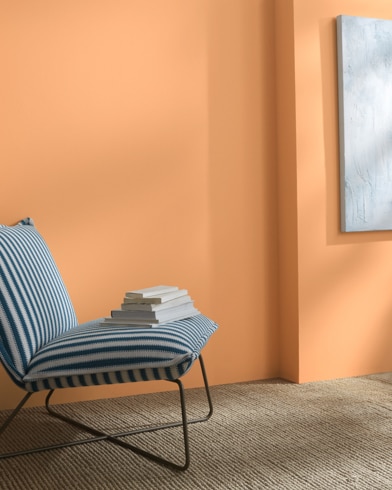 A Vivid Beauty-painted wall behind a striped armless lounge chair with books on it. 