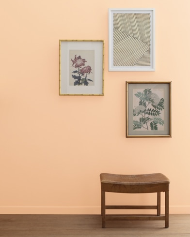 ACreamy Orange-painted wall with three framed art pieces, a small bench, and a floor lamp.