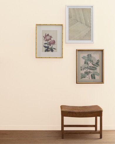 A Gentle Repose-painted wall with three framed art pieces, a small bench, and a floor lamp.